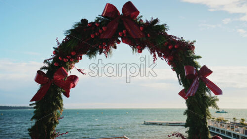 Video - Decorative Christmas arch adorned with greenery, red bows, and ornaments, set against the Mediterranean Sea