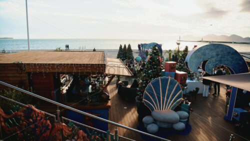 Video - Cannes, France - December 23, 2025: Festive Christmas village set directly on the beachfront, featuring decorated trees, holiday installations, and visitors at a restaurant