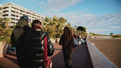 Video - Cannes, France - December 23, 2025: Pedestrians walking along La Croisette on a sunny day, with palm trees, benches, and the Mediterranean Sea in the background