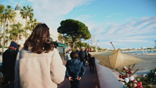 Video - Cannes, France - December 23, 2025: People walking by a golden Christmas star decoration attached to a seafront railing along La Croisette