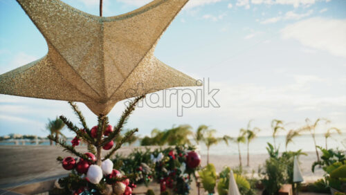 Video - Close up of a golden Christmas star decoration with blurred palm trees and beach in the background