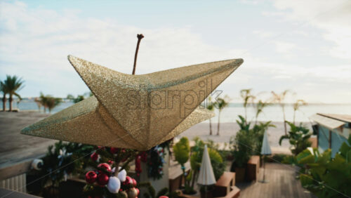 Video - Close up of a golden Christmas star decoration with blurred palm trees and beach in the background