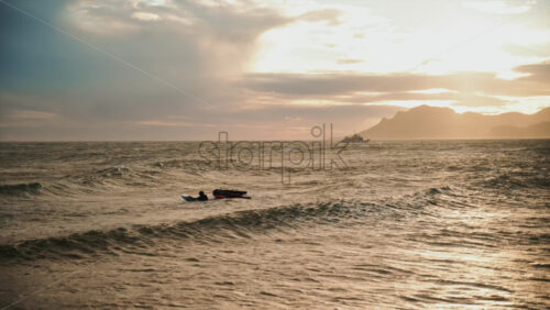 Video - Single surfer resting on a board in choppy Mediterranean waters during sunset