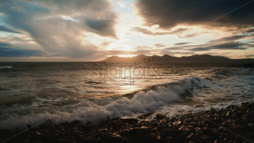 Video - Evening waves washing over a rocky shoreline under dramatic clouds and warm sunset light