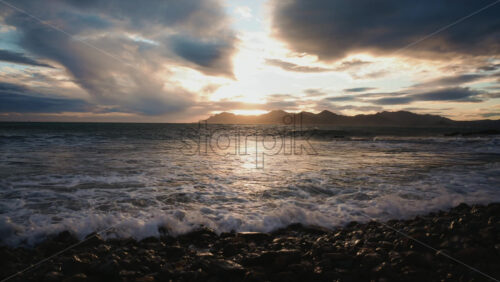 Video - Evening waves washing over a rocky shoreline under dramatic clouds and warm sunset light