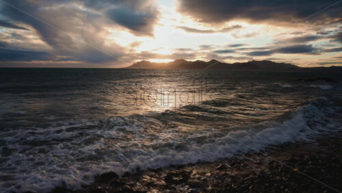 Video - Evening waves washing over a rocky shoreline under dramatic clouds and warm sunset light