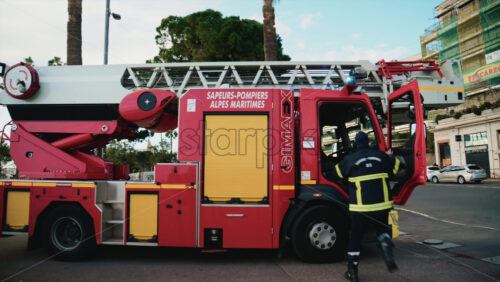 Video - Cannes, France - December 23, 2025: Red fire truck driving along La Croisette with palm trees and pedestrians in the background