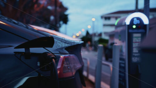 Video - Black, electric car plugged into a public charging station during evening hours