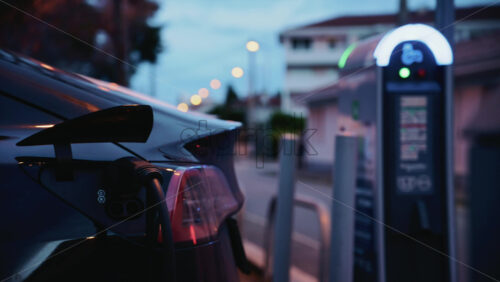 Video - Black, electric car plugged into a public charging station during evening hours