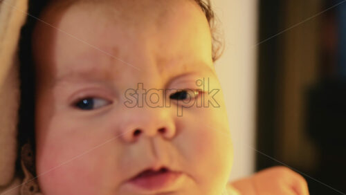 Video - Close up of a baby's face with blue eyes and smooth, rosy skin with festive golden bokeh lights in the background