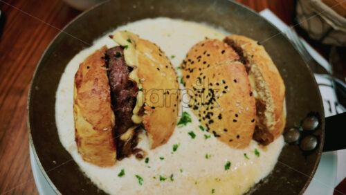 Video - Two small beef sliders served in a shallow pan, resting in a creamy white sauce
