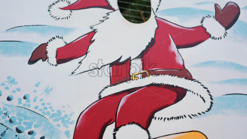 Video - A painted cutout board depicting Santa Claus in a red suit with white trim, arms spread wide on a yellow snowboard