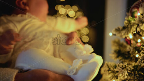 Video - Baby being held close to a decorated Christmas tree, reaching toward illuminated ornaments and lights