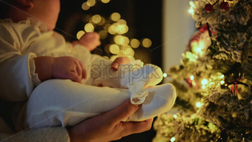 Video - Baby being held close to a decorated Christmas tree, reaching toward illuminated ornaments and lights
