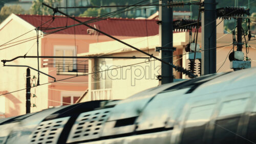 Video - Close up of an electric train passing beneath overhead power lines and utility structures