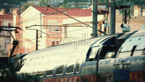 Video - Close up of an electric train passing beneath overhead power lines and utility structures