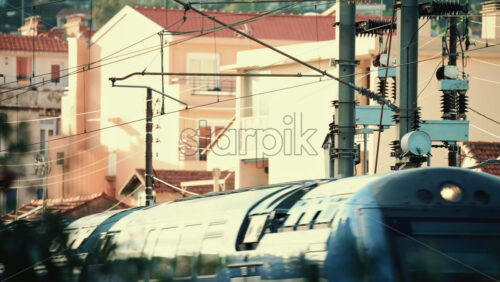 Video - Close up of an electric train passing beneath overhead power lines and utility structures