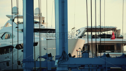 Video - Large white yachts positioned inside a blue metal lifting structure at a marina or shipyard