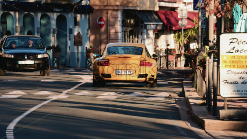 Video - Vallauris, France - December 27, 2025: Rear view of a yellow sports car driving along a narrow town street