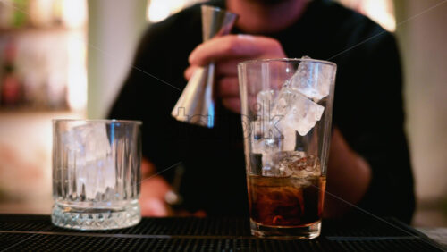 Video - A bartender pours a spirit from a metal jigger into a tall glass filled with clear ice cubes