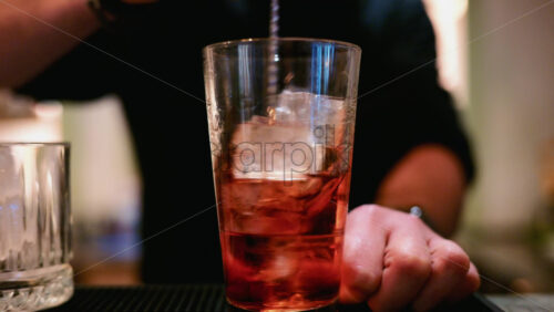 Video - Close up of a bartender stirring a red cocktail with a long bar spoon in a highball glass