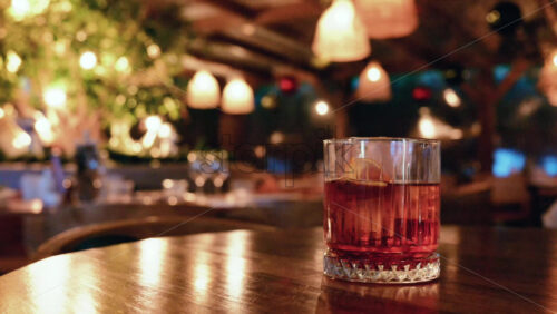 Video - Glass of red cocktail placed on a wooden table inside a warmly lit restaurant