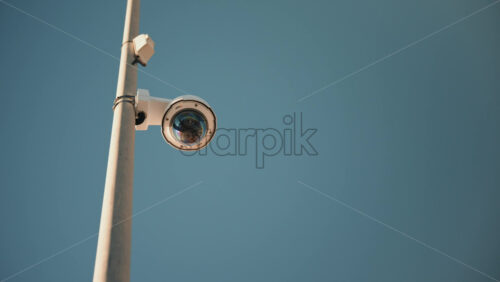 Video - Vallauris, France - December 29, 2025: Modern street surveillance camera mounted on a metal pole against a clear blue sky