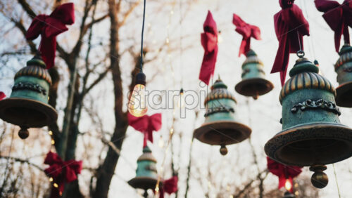 Video - Decorative hanging bells with red bows and warm string lights outdoors