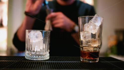Video – A bartender pours a spirit from a metal jigger into a tall glass filled with clear ice cubes - Starpik Stock