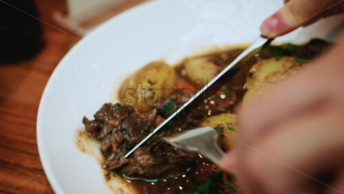 Video – A close up of a hand using a knife and fork to cut into tender pieces of beef in a stew - Starpik Stock