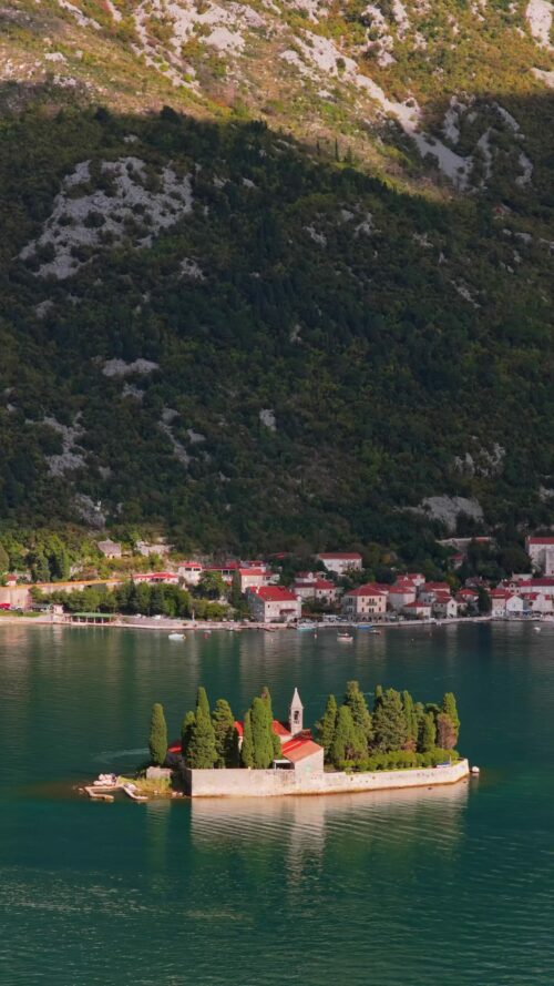 Video – Aerial drone view of the small natural island of Saint George, featuring a stone monastery surrounded by tall cypress trees on turquoise water. Vertical - Starpik Stock