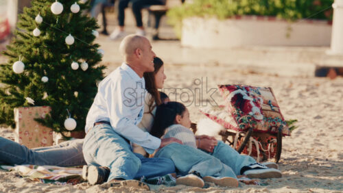 Video – Antibes, France – December 17, 2025: Family taking pictures on a blanket near a decorated Christmas tree on a sandy beach - Starpik Stock
