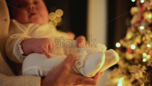 Video – Baby being held close to a decorated Christmas tree, reaching toward illuminated ornaments and lights - Starpik Stock