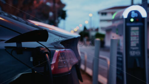 Video – Black, electric car plugged into a public charging station during evening hours - Starpik Stock