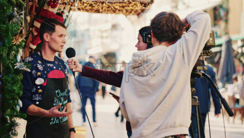 Video – Cannes, France – December 20, 2025: Man being interviewed on camera at a festive Christmas market decorated with lights and garlands - Starpik Stock