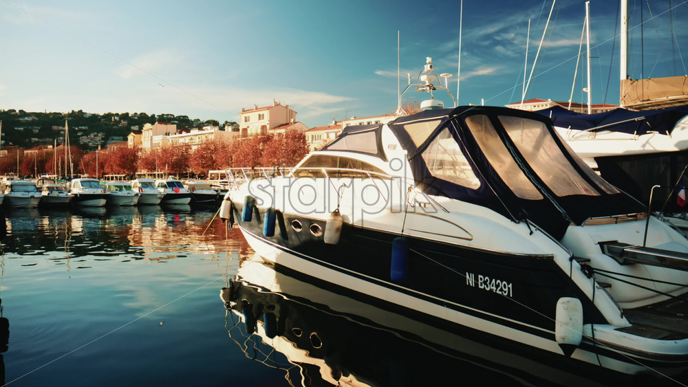 Video – Cannes, France – December 22, 2025: A modern motor yacht moored at a harbor, with autumn colored trees and residential buildings lining the waterfront in the background - Starpik Stock