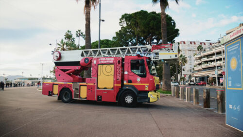 Video – Cannes, France – December 23, 2025: Red fire truck driving along La Croisette with palm trees and pedestrians in the background - Starpik Stock