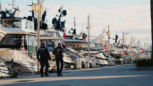 Video – Cannes, France – December 23, 2025: Two uniformed police officers walking along a marina promenade with luxury yachts docked in the background - Starpik Stock