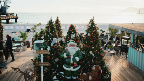 Video – Cannes, France – December 23, 2025: Wide view of a busy restaurant decorated for Christmas by the sea with decorated trees, holiday installations, and visitors - Starpik Stock