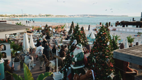 Video – Cannes, France – December 23, 2025: Wide view of a busy restaurant decorated for Christmas by the sea with decorated trees, holiday installations, and visitors - Starpik Stock