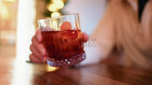Video – Close up of a hand holding a glass filled with a red cocktail, ice cubes, and citrus peel - Starpik Stock