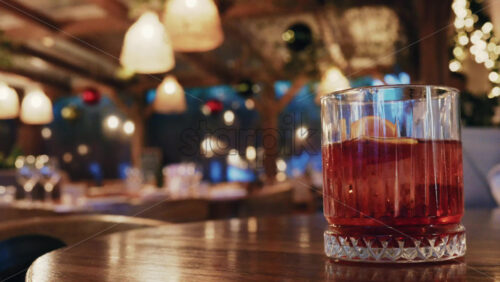 Video – Glass of red cocktail placed on a wooden table inside a warmly lit restaurant - Starpik Stock