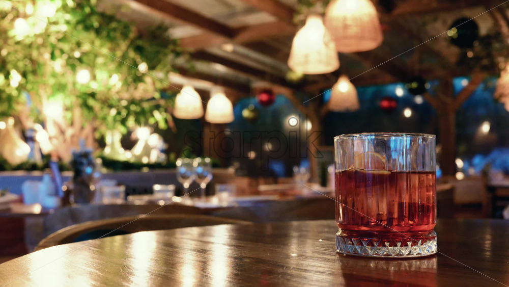 Video – Glass of red cocktail placed on a wooden table inside a warmly lit restaurant - Starpik Stock