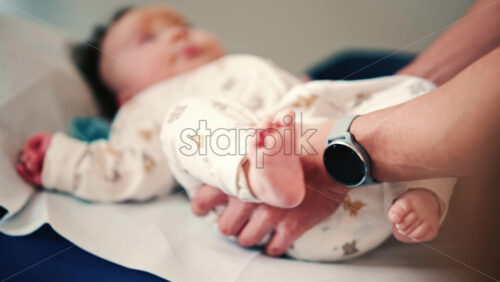 Video – Infant lying on a padded examination table while caregivers gently support the body during a routine check - Starpik Stock