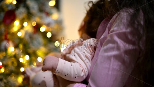 Video – Mother holding a baby indoors next to a decorated and illuminated Christmas tree - Starpik Stock