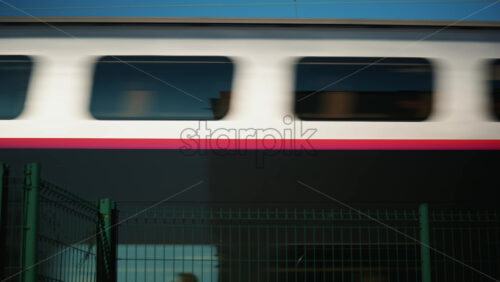 Video – Side view of a passenger train moving past a green fence near the railway tracks - Starpik Stock