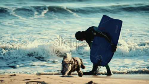 Video – Vallauris, France – December 27, 2025: Surfer in a wetsuit bending down on the shoreline to adjust fins while holding a surfboard - Starpik Stock