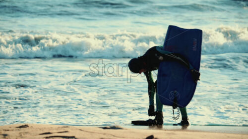 Video – Vallauris, France – December 27, 2025: Surfer in a wetsuit bending down on the shoreline to adjust fins while holding a surfboard - Starpik Stock
