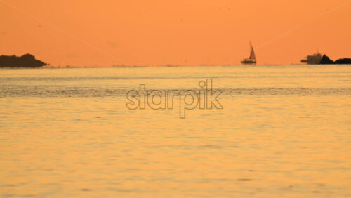 Video – Wide seascape showing a distant vessel on the horizon beneath an orange sunset sky, with calm water - Starpik Stock