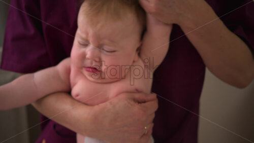 Infant lying face down across a caregiver's forearm, supported securely